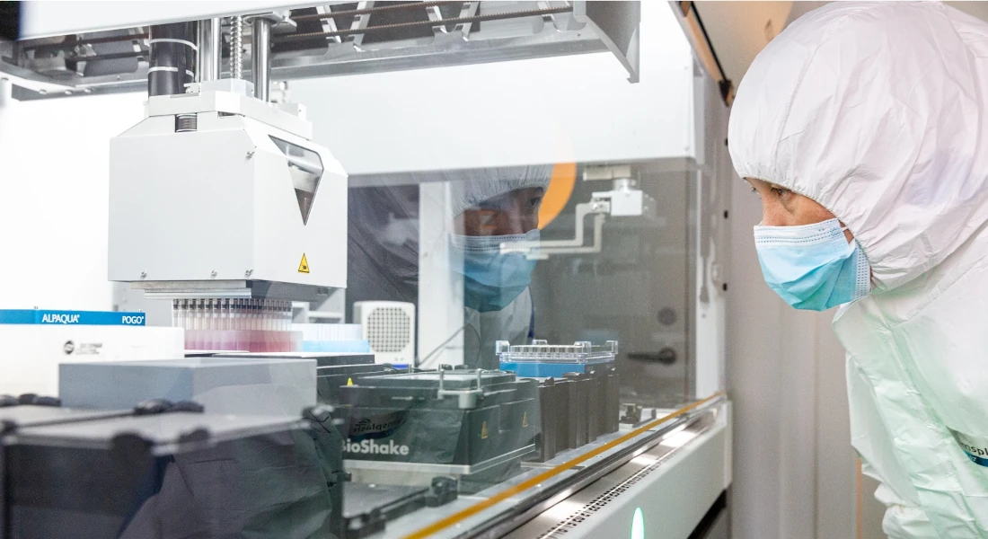 Scientist wearing lab-clothes overseeing machine treating samples in lab.