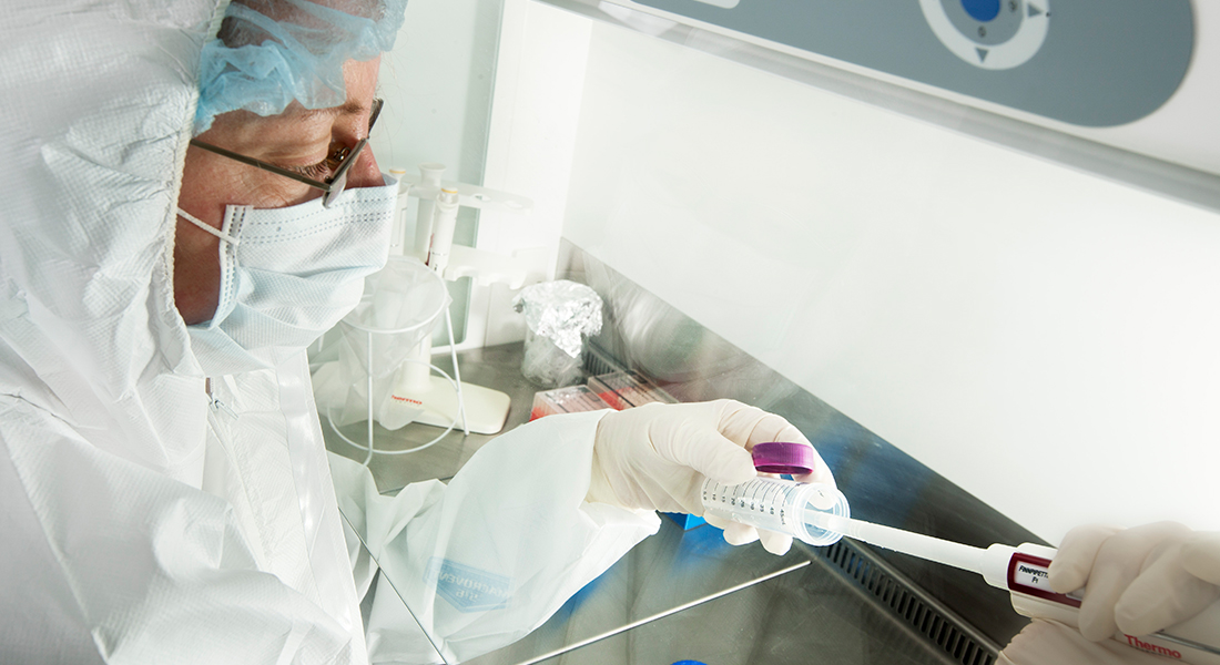 Close-up of researcher working in lab, wearing protective clothing and mask.