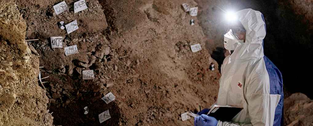 Researchers collecting samples in cave wearing protective gear and headlamps.